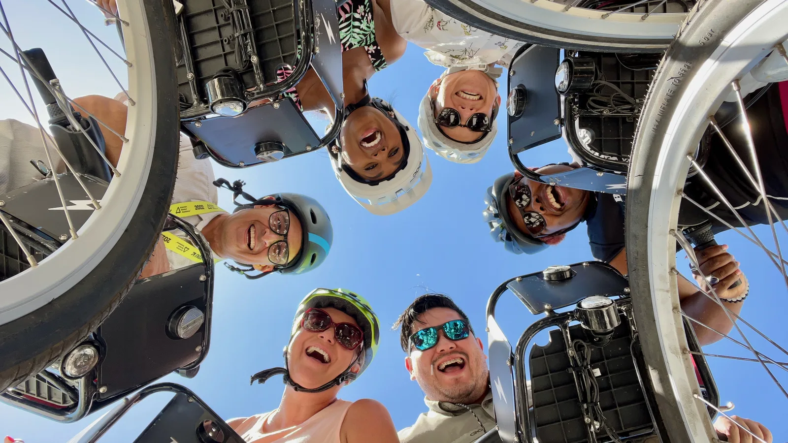 Group of people smiling at camera over the handlebars of their bike share bicycles.