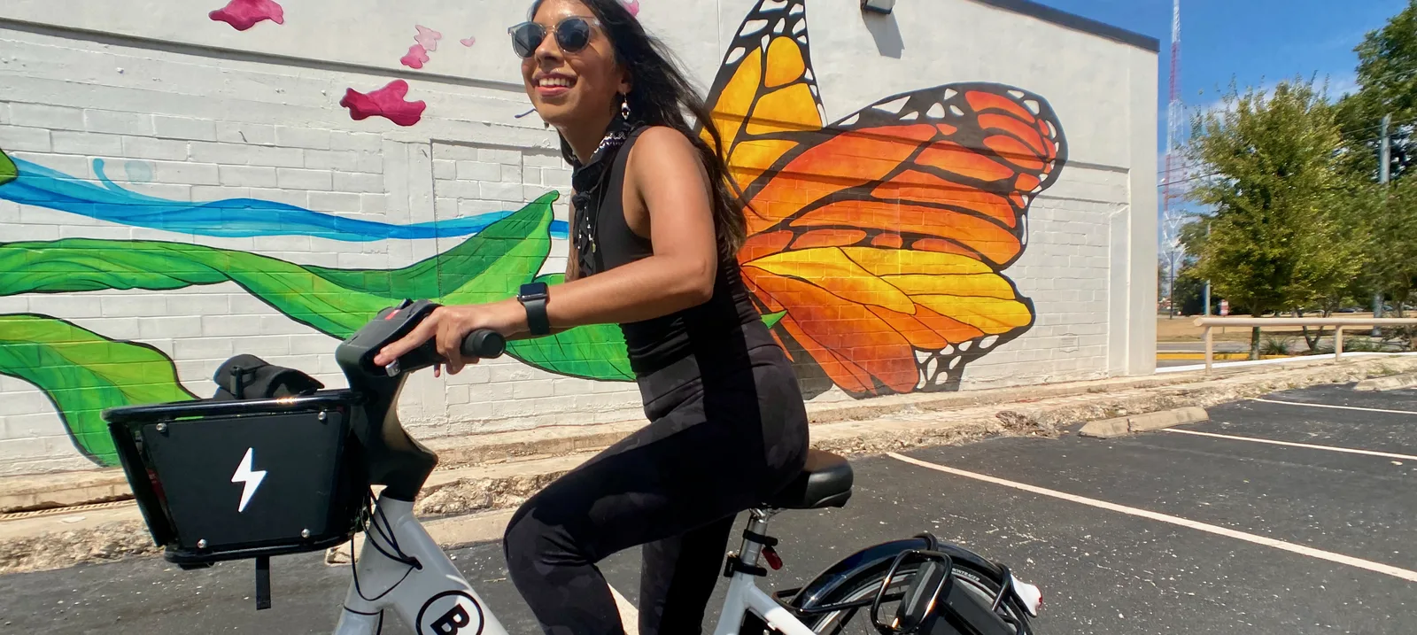 Latina woman riding a bike share bicycle in front of Monarch butterfly mural