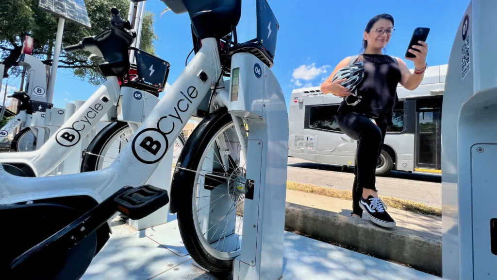 Latino woman walking to the bike share station while using her BCycle app on her smart phone.