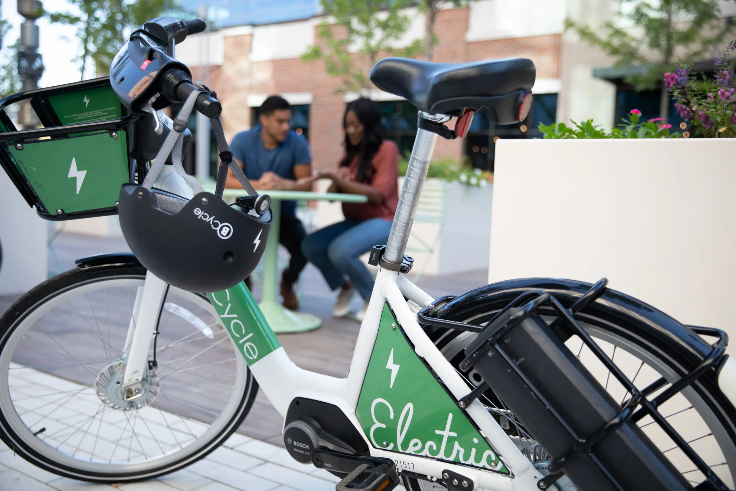 Couple sitting down at outdoor table next to a bike share bicycle.