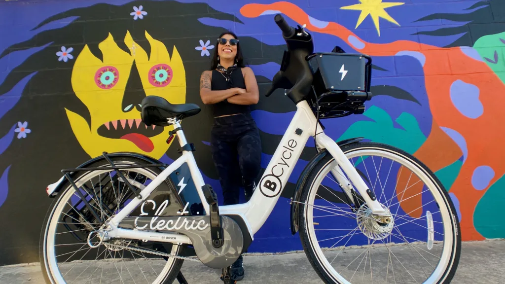 Latina woman leaning against mural beside her bike share bicycle